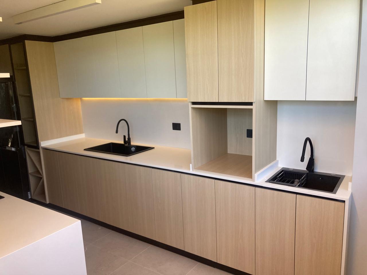 Cocina a medida con mueblería en madera clara, cubierta blanca y grifería negra